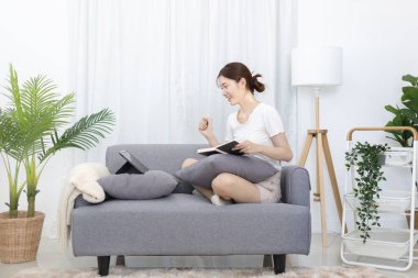 Asian woman taking notes in notebook while studying online in laptop at home, Video chat, Online communication , Stay home, New normal, Distance learning, Live show online, Learn online, living room.