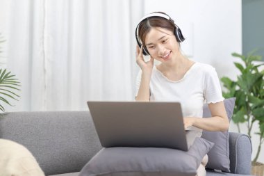 Beautiful Asian woman sits happily listening to music in the living room, Chill, Relaxation time, Happy time, Feel good, Happy weekend getaway, Favorite sofa or Comfort Zone, Feel good.