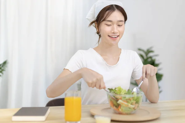 Asian woman eating salad on the dining table smiling and happy, Vegetable salads are rich in vitamins and minerals, Fat-low-calorie and high-fiber diets, Health care by eating fresh vegetables.