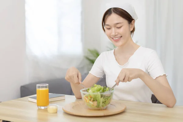 Asian woman eating salad on the dining table smiling and happy, Vegetable salads are rich in vitamins and minerals, Fat-low-calorie and high-fiber diets, Health care by eating fresh vegetables.