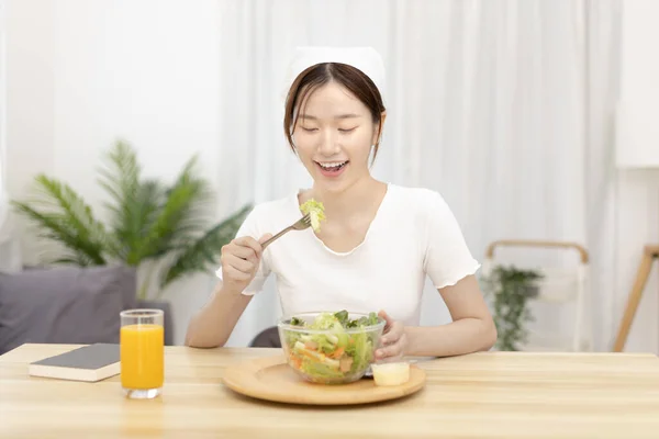 Asian woman eating salad on the dining table smiling and happy, Vegetable salads are rich in vitamins and minerals, Fat-low-calorie and high-fiber diets, Health care by eating fresh vegetables.