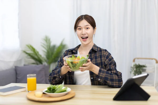 Asian woman eating salad on the dining table smiling and happy, Vegetable salads are rich in vitamins and minerals, Fat-low-calorie and high-fiber diets, Health care by eating fresh vegetables.