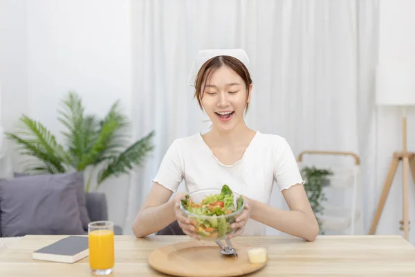 Asian woman eating salad on the dining table smiling and happy, Vegetable salads are rich in vitamins and minerals, Fat-low-calorie and high-fiber diets, Health care by eating fresh vegetables.