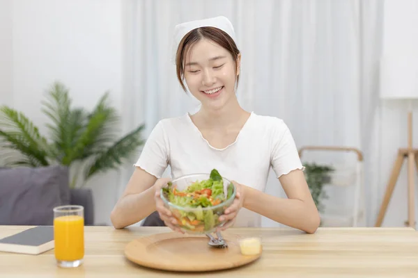 Asian woman eating salad on the dining table smiling and happy, Vegetable salads are rich in vitamins and minerals, Fat-low-calorie and high-fiber diets, Health care by eating fresh vegetables.