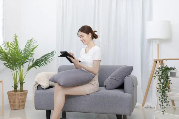 Asian Woman Sitting Sofa Tablet Looking Tablet Screen Relaxing Home — Stok fotoğraf