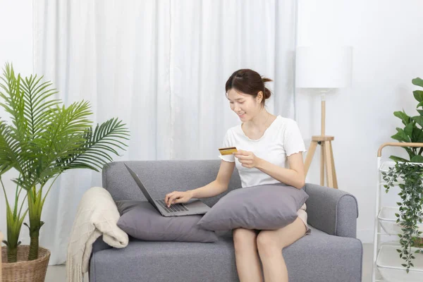 Asian woman lounging on sofa and using laptop to shop online with credit card to register for payment or online transactions, Financial transactions and Internet security, Shopping with credit card.