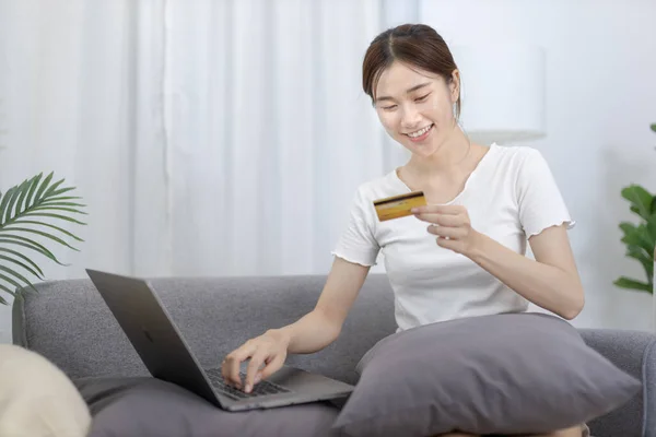 Asian woman lounging on sofa and using laptop to shop online with credit card to register for payment or online transactions, Financial transactions and Internet security, Shopping with credit card.