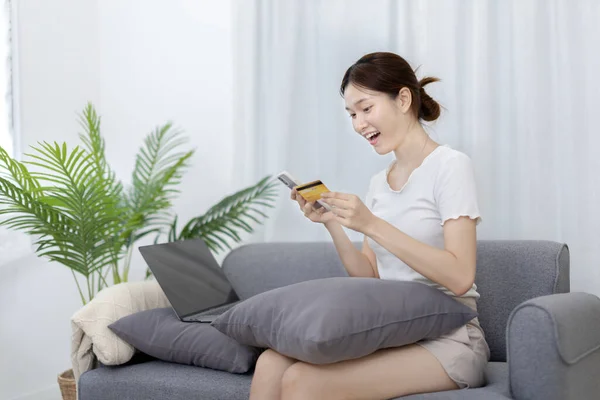 Asian woman sitting on sofa and using phone to shop online with credit card to register for payment or online transactions, Financial transactions and Internet security, Shopping with credit card.