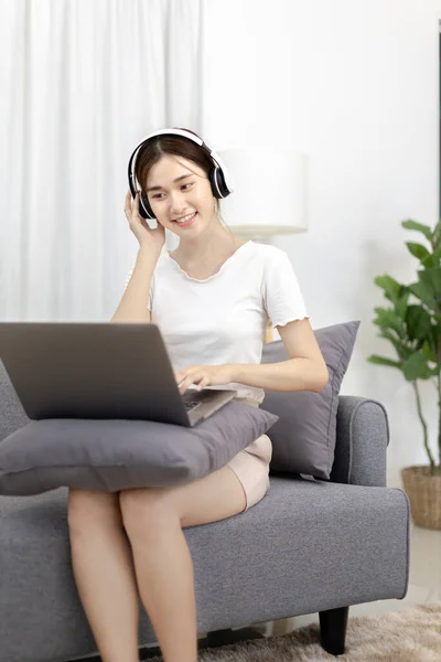 Beautiful Asian woman sits happily listening to music in the living room, Chill, Relaxation time, Happy time, Feel good, Happy weekend getaway, Favorite sofa or Comfort Zone, Feel good.