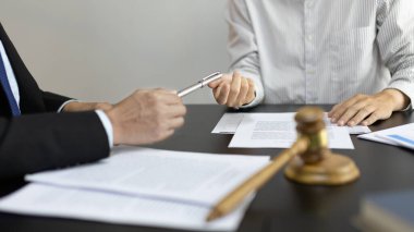 Avukat ya da avukat müvekkiline bir iş sözleşmesi imzalaması için kalem veriyor, sözleşmeyi şartlara ve şartlara göre imzalıyor, adalet terazisi, hukuki çekiç, dava kavramı ve hukuki hizmet kavramı