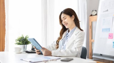 Çalışmak için dizüstü bilgisayar kullanan iş kadını, ofiste çalışan Asyalı kadın, evrak ve ekipmanlarla çalışan muhasebeci, mali işlemler için tablet kullanan.