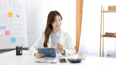 Çalışmak için dizüstü bilgisayar kullanan iş kadını, ofiste çalışan Asyalı kadın, evrak ve ekipmanlarla çalışan muhasebeci, mali işlemler için tablet kullanan.