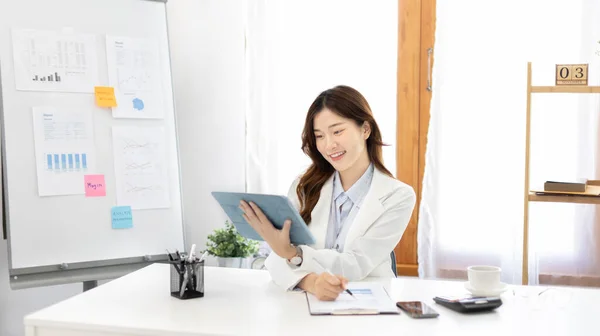 Businesswoman using laptop to work, Asian woman working in the office, Financial clerk or accountant with documents and equipment working on the desk, Using tablet for financial transactions.