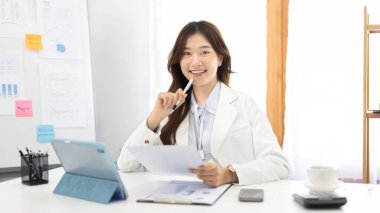 Çalışmak için dizüstü bilgisayar kullanan iş kadını, ofiste çalışan Asyalı kadın, evrak ve ekipmanlarla çalışan muhasebeci, mali işlemler için tablet kullanan.