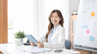 Çalışmak için dizüstü bilgisayar kullanan iş kadını, ofiste çalışan Asyalı kadın, evrak ve ekipmanlarla çalışan muhasebeci, mali işlemler için tablet kullanan.