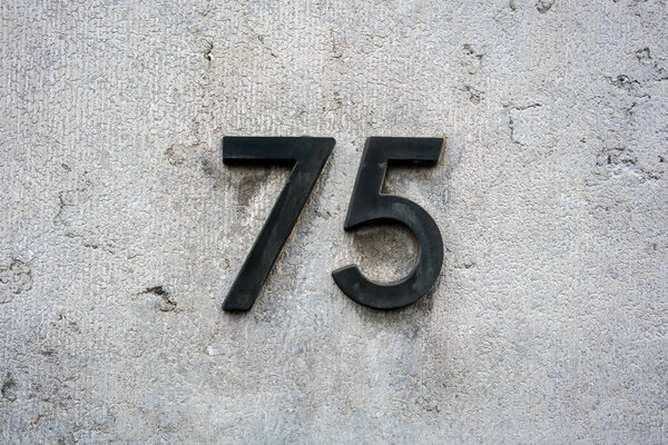 Black house number seventy five (75) on a concrete wall