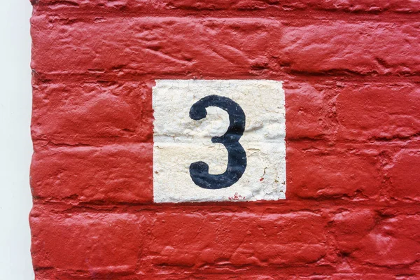 hand painted house number three on a red painted wall