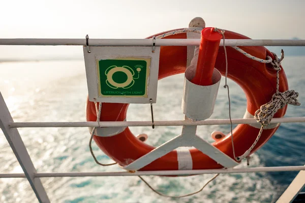Boya salvavidas con letrero en una valla de ferry, con sol y mar en backgro — Foto de Stock