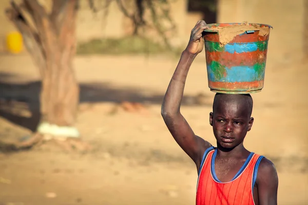 Unidentified boy carrying clay in wooden vessel on his head, — Stock Photo, Image