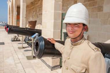 Boy dressed as in old English military uniform in front of the cannons in Valletta, Malta clipart