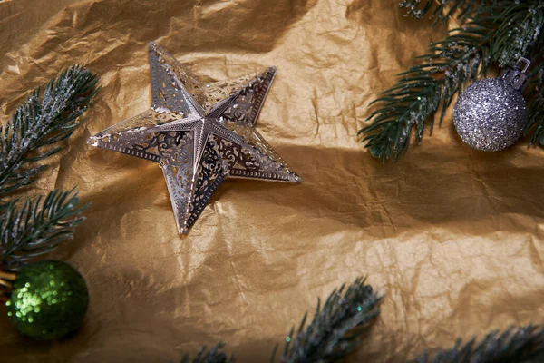Altın buruşuk kağıt arka planda noel kompozisyonu. Köknar topları ve köknar dalları ile gümüş yıldız, üst görünüm.