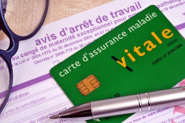 Fransız sağlık sigortası kartı iş durdurma formunun üzerine yerleştirilmiş gözlük ve kalemin yanına.