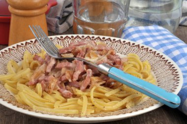 Pastırmalı linguine tabağı ve bir bardak suyun yanında çatal. 