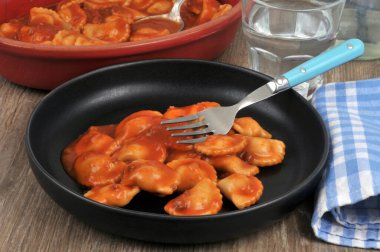 Masada bir tabak ravioli, yanında bir çatal ve bir bardak su ile servis edilir.