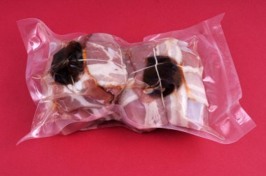 Kırmızı zemin üzerinde vakumlu plastik ambalaj içinde kuru erikli ham dana eti ruloları