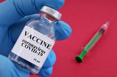 Coronavirus aşısı kavramı. Elinde şişe ve kırmızı arka planda şırınga var.