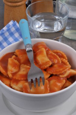 Çatalla servis edilen bir kasede domates soslu ravioli. 