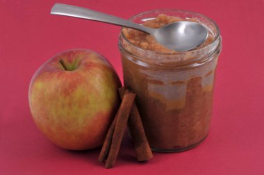 Tarçın çubuklu elma ve kırmızı arka planda bir kavanoz komposto.