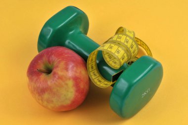 Dambılı bir elma ve sarı arka planda esnek bir mezura.