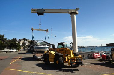 Forklift ve iskele vinci Dinard marinasında bir tekne kaldırıyor.
