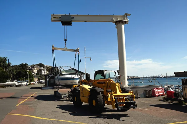 Forklift ve iskele vinci Dinard marinasında bir tekne kaldırıyor.