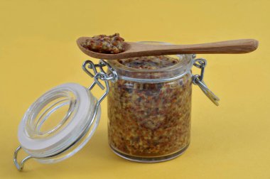 Bir kaşık dolusu eski moda hardal sarı arka planda bir hardal kavanozunun üzerinde dinleniyor.