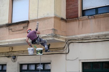 Bir binanın ön cephesinde çalışan halatlı bir ressam.