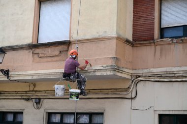 Bir binanın ön cephesinde çalışan halatlı bir ressam. 