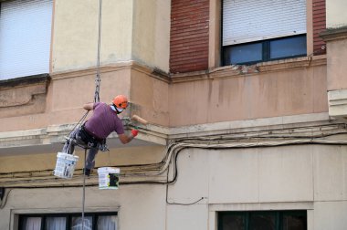 Bir binanın ön cephesinde çalışan halatlı bir ressam. 