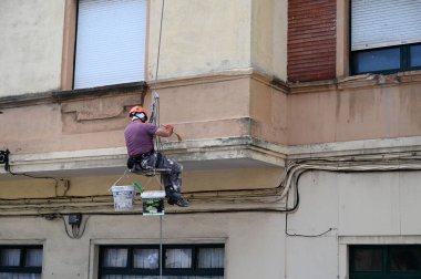 Bir binanın ön cephesinde çalışan halatlı bir ressam.