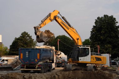 Kazıcı inşaat alanına çöp kamyonu yüklüyor.