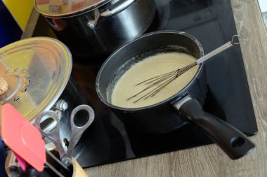 Preparing a bechamel sauce in a saucepan with a kitchen whisk on a hob