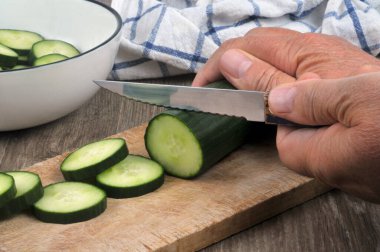 Cut a cucumber into rings with a knife on a cutting board 
