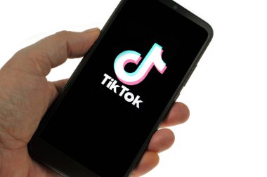 TikTok application on smartphone held in hand close up on white background | Application TikTok sur un smartphone tenu en main en gros plan sur fond blanc