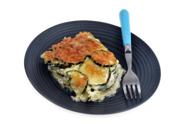 Beyaz arka planda çatalla kaplanmış bir tabakta kabak graten.