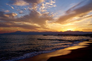 Beautiful sunset over the sea or ocean. Bright and soft colors, magic light. Small clouds in the sky, the reflection of the sun in the water and sand on the beach. The concept of romantic time on vacation in the tropic.                               