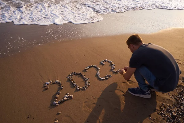 2022 'de kumsalda yazan adam. Okyanus dalgası ve plajdaki harfler. Mutlu yıllar 2022 tropikal tatil 2022, yeni bir başlangıç. 2022 'ye yeni çözümler ve hayaller konseptiyle hoş geldiniz..