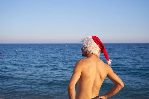 戴着圣诞礼帽的年轻人住在海滩附近 热带沙滩季节性旅游度假 蓝天背景户外 寒假背景图 — 图库照片