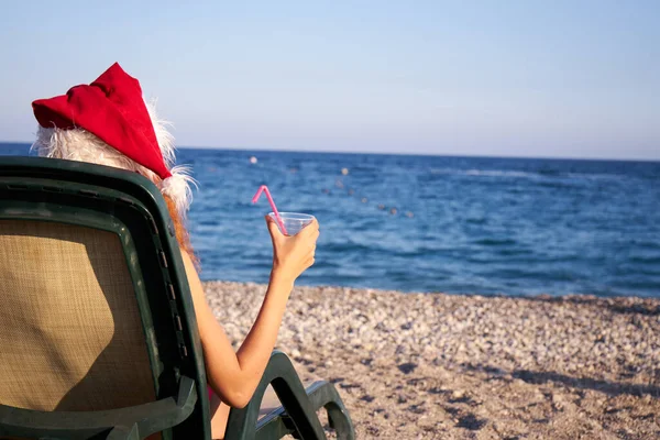 美丽的红头发女人头戴圣诞帽 身穿粉色比基尼 在海边享受寒假 圣诞节或新年假期在海滨的豪华度假胜地 旅行女孩喝燕尾服 免版税图库照片