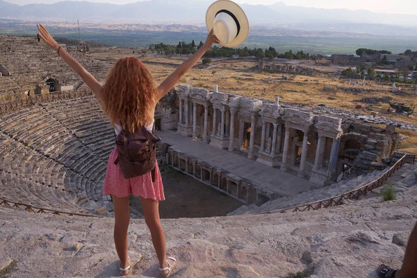 Hierapolis antik kenti Pamukkale Türkiye, Unesco harabelerinde günbatımını izleyen şapkalı genç bir kadın. Pamukkale 'nin antik kenti Hierapolis tiyatrosunda ayakta duran gezgin kadın                               